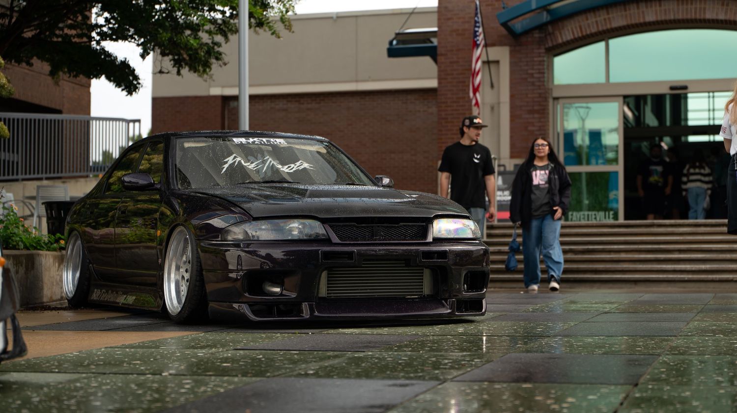 Car enthusiasts gather at an outdoor meet with modified vehicles and sports cars on display.