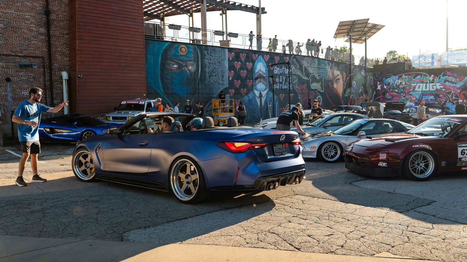 Row of customized sports cars displayed in front of an urban building with street art.