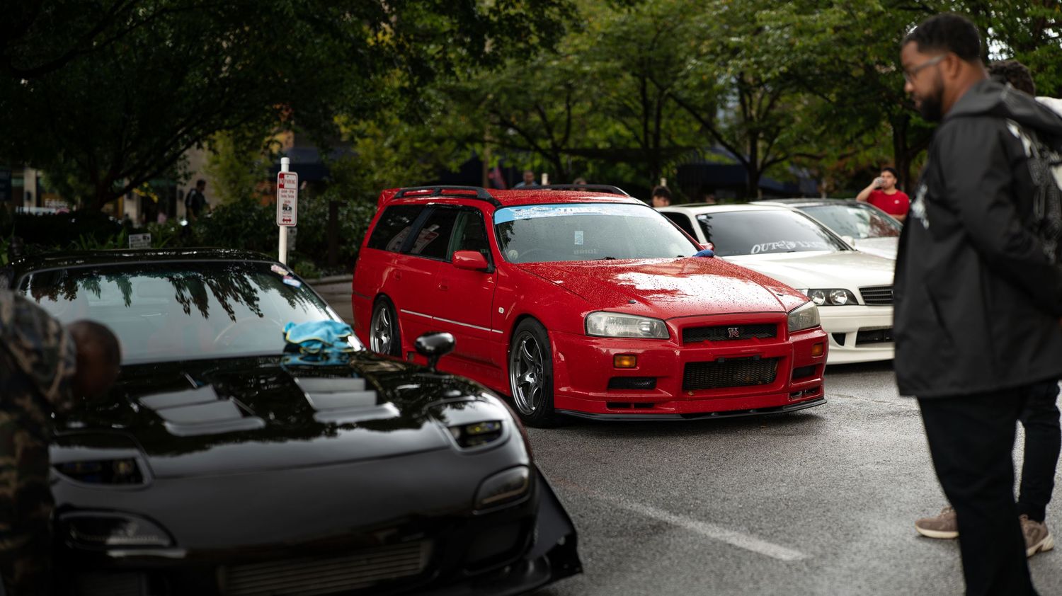 Wide shot of a car meet showing various performance vehicles in a parking area.