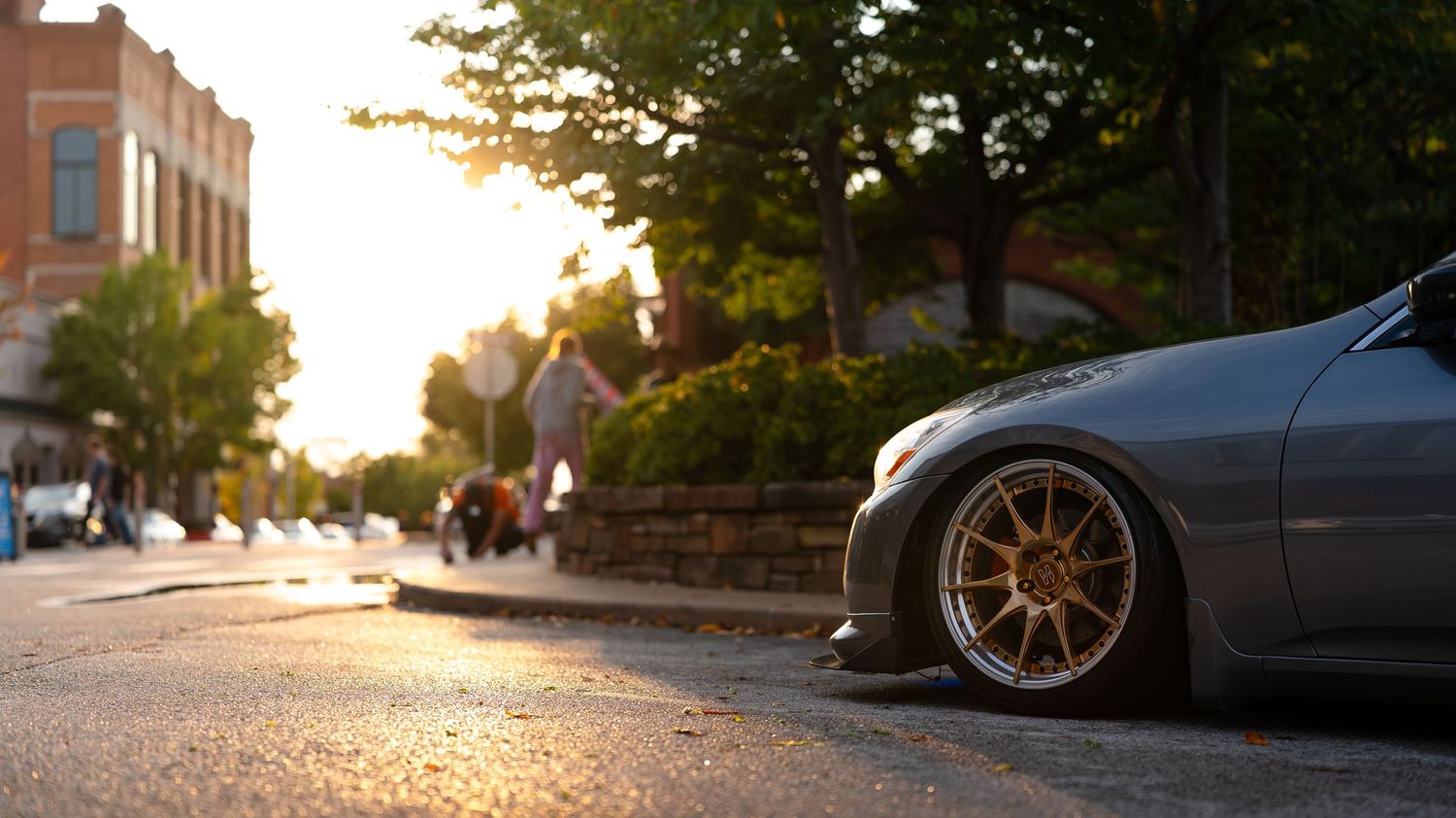 Car enthusiasts gather at sunset for a meet-up in an urban area with parked vehicles.
