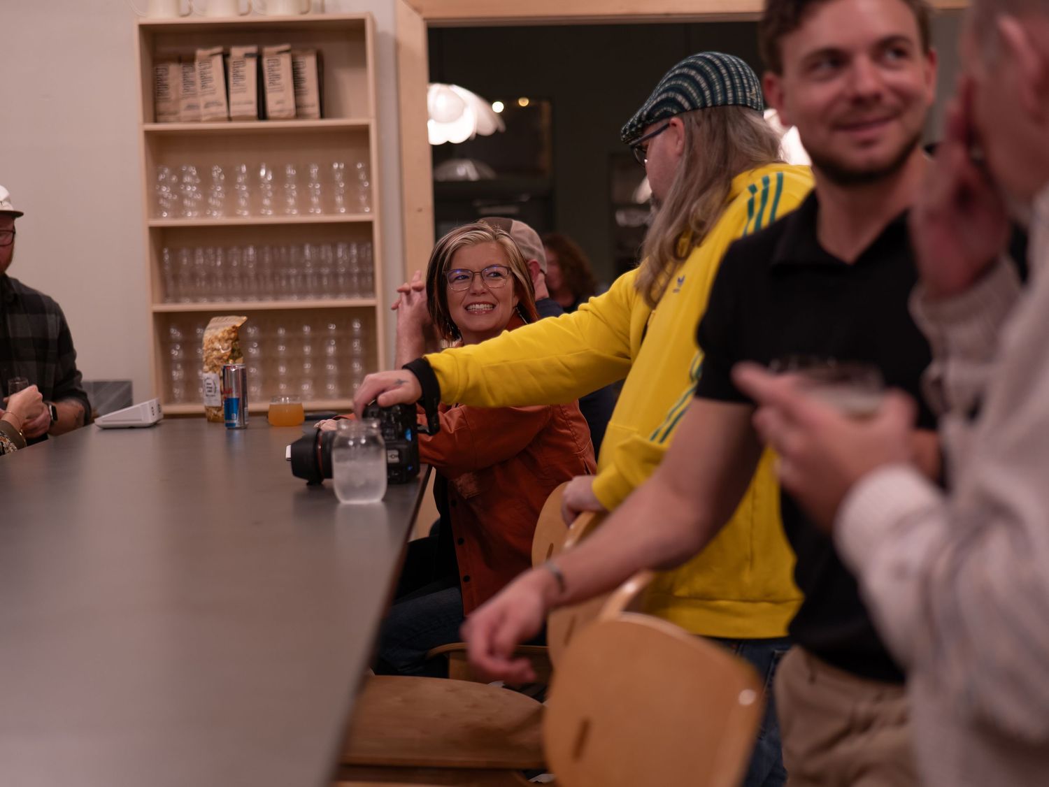 People in yellow and white shirts sit at a table playing a tabletop game with wooden pieces.