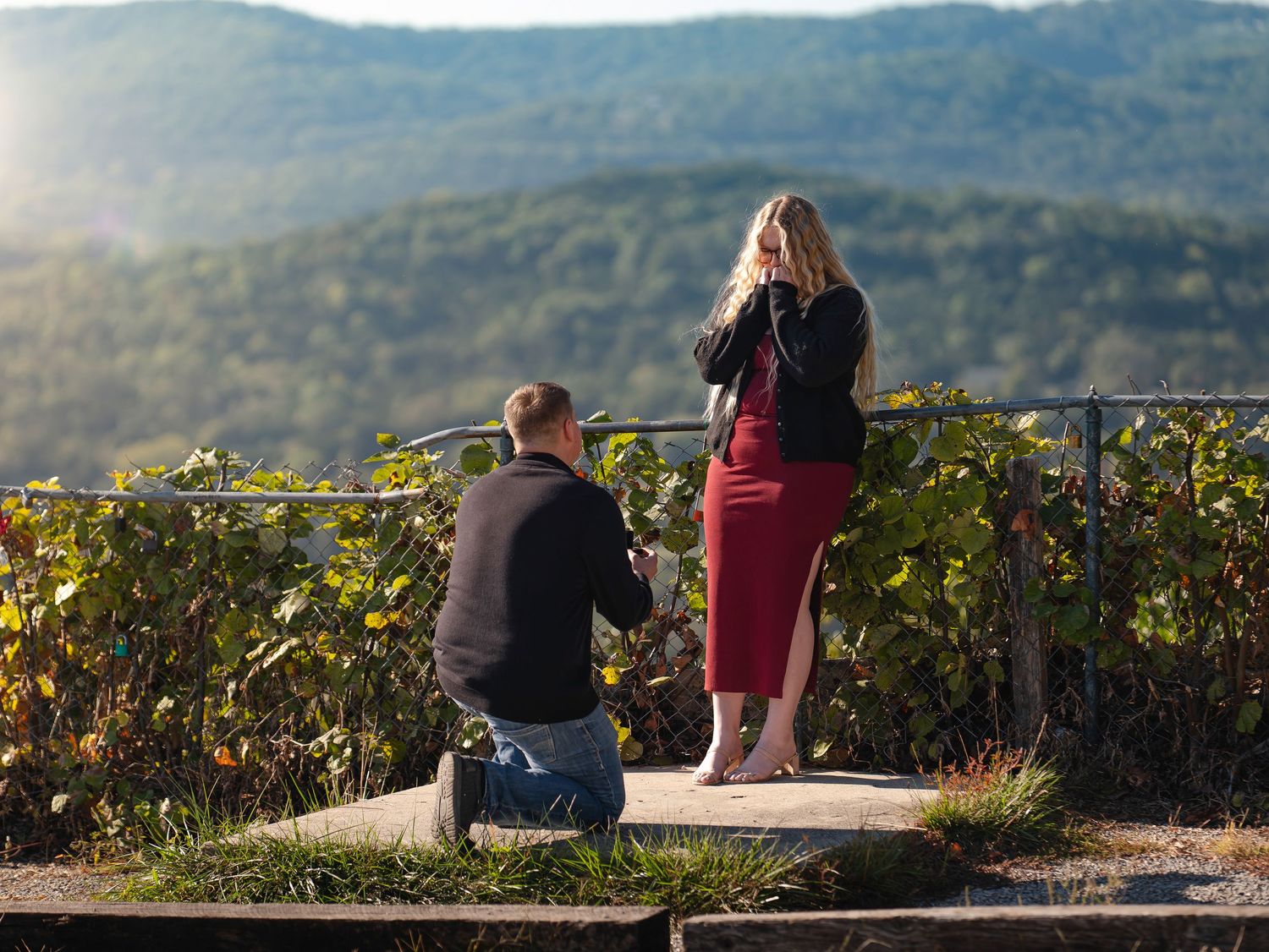 People sitting on a hillside overlook enjoying mountain views at sunset.