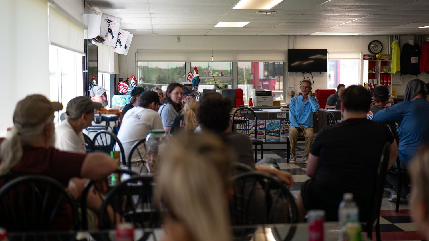 Crowded indoor gathering space with fluorescent lighting and people seated at tables.