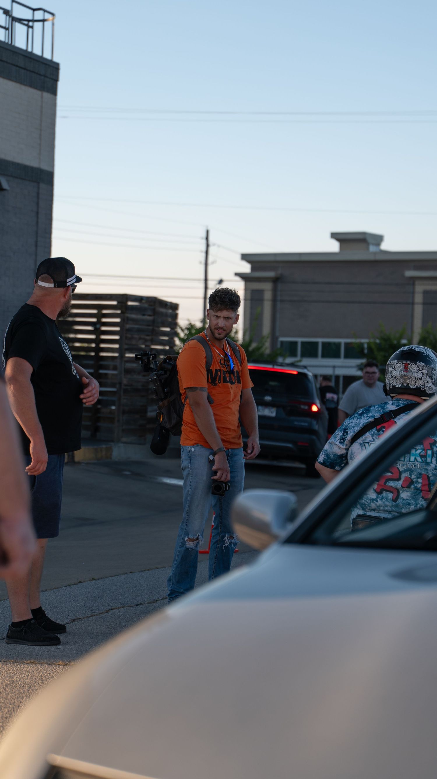 Group gathered around cars in a parking lot during evening hours.