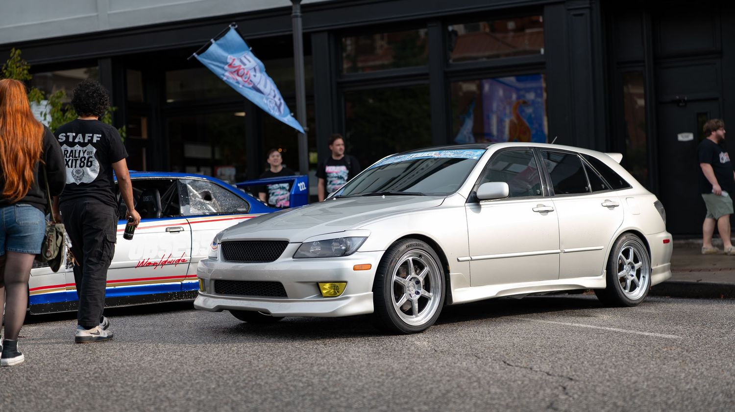 Street scene with modified cars and spectators gathered at an automotive event.