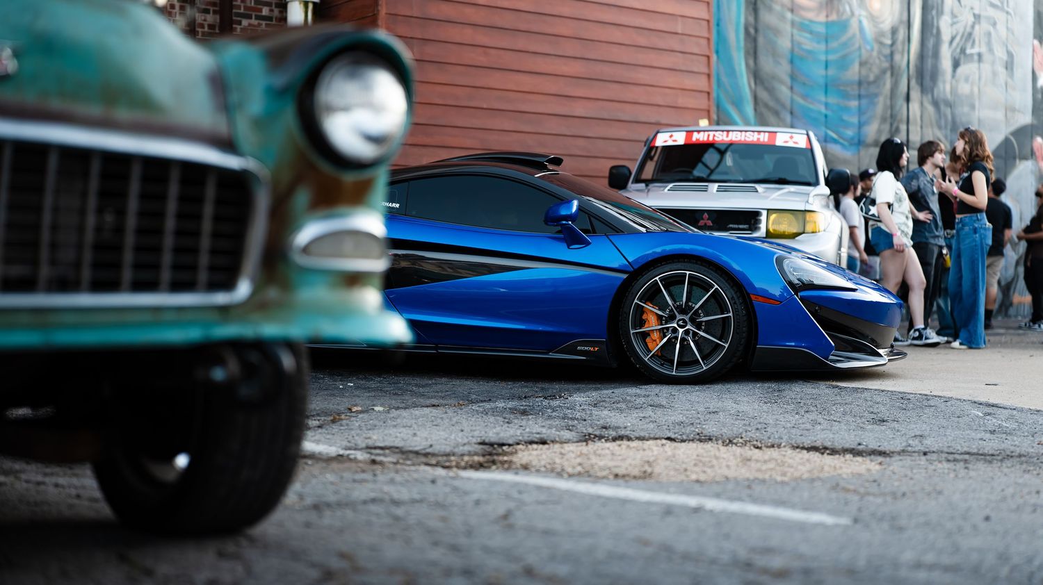 Low-angle view of performance cars parked along a brick building exterior.