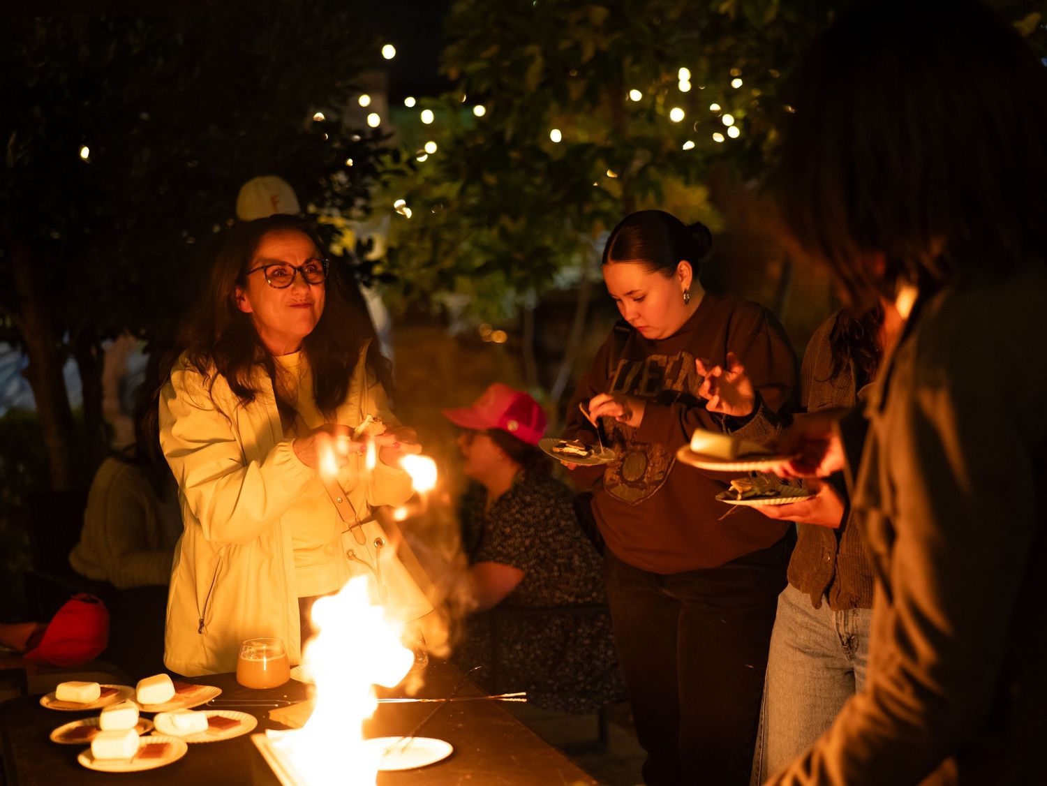 People gather around glowing candles at a nighttime outdoor event creating a warm and intimate atmosphere.