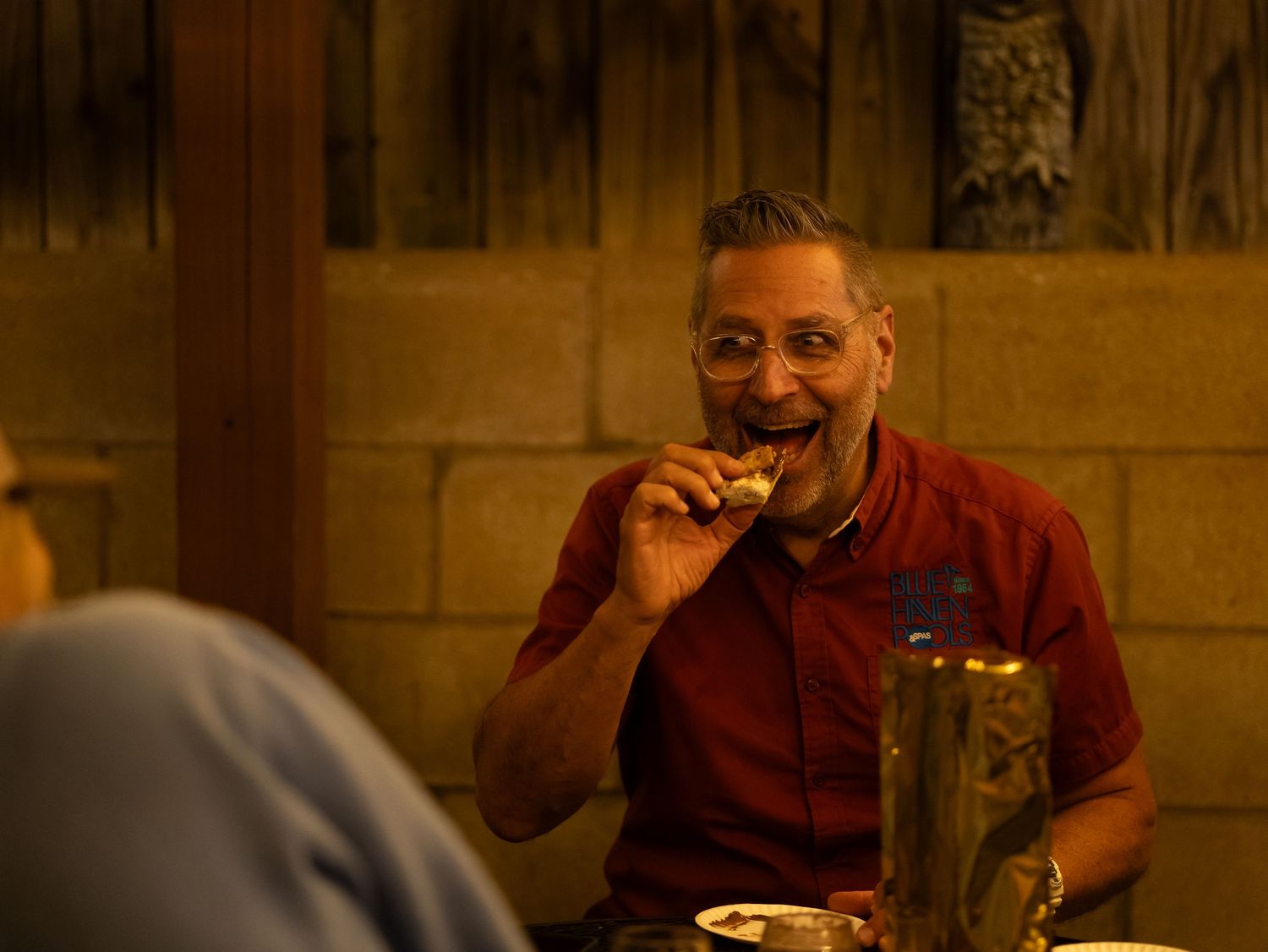 A person in a burgundy shirt enjoys a meal at a restaurant table.