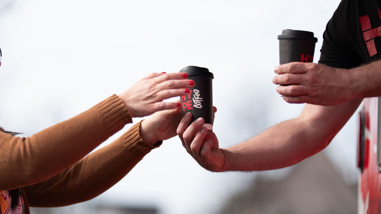 Close-up of hands passing drinks between people outdoors.