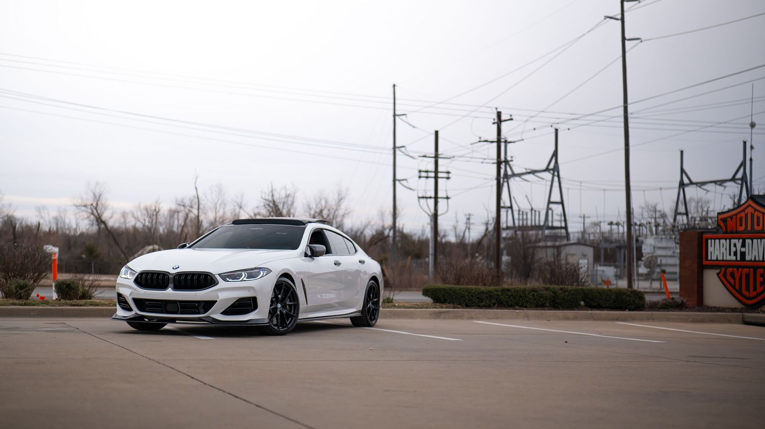 White BMW M850i sedan parked in an industrial area with power lines in the background.