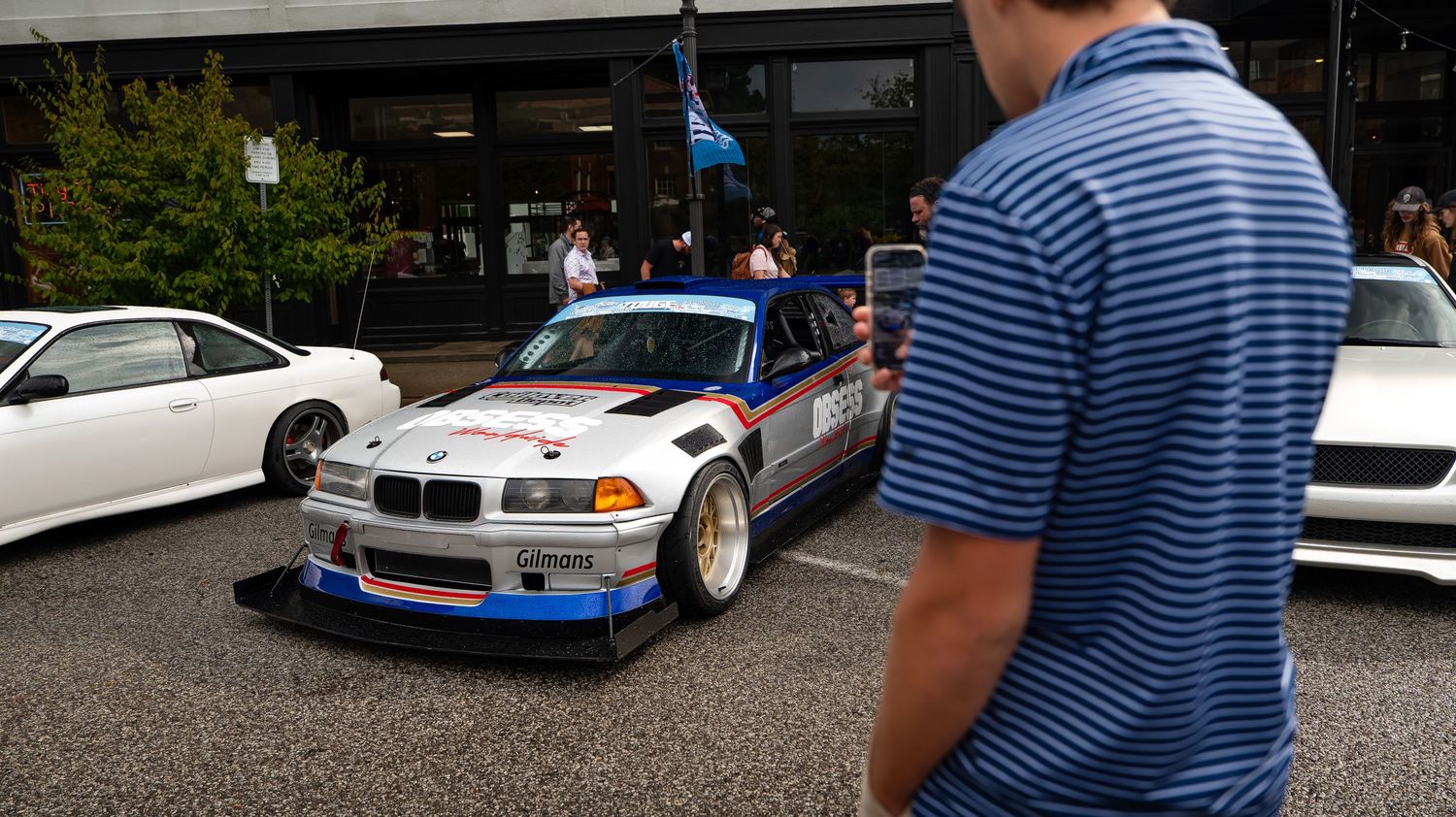 Row of modified cars parked at a car show with spectators viewing the vehicles.