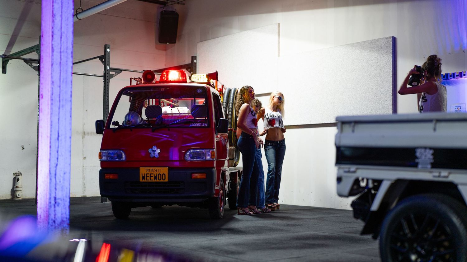 Police cars and vehicles parked in a dimly lit indoor parking garage with purple lighting.