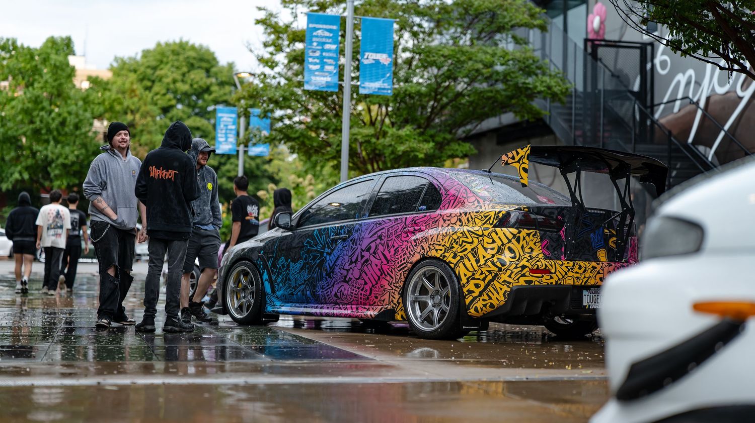Rain-soaked parking area with cars and trees visible in the background.
