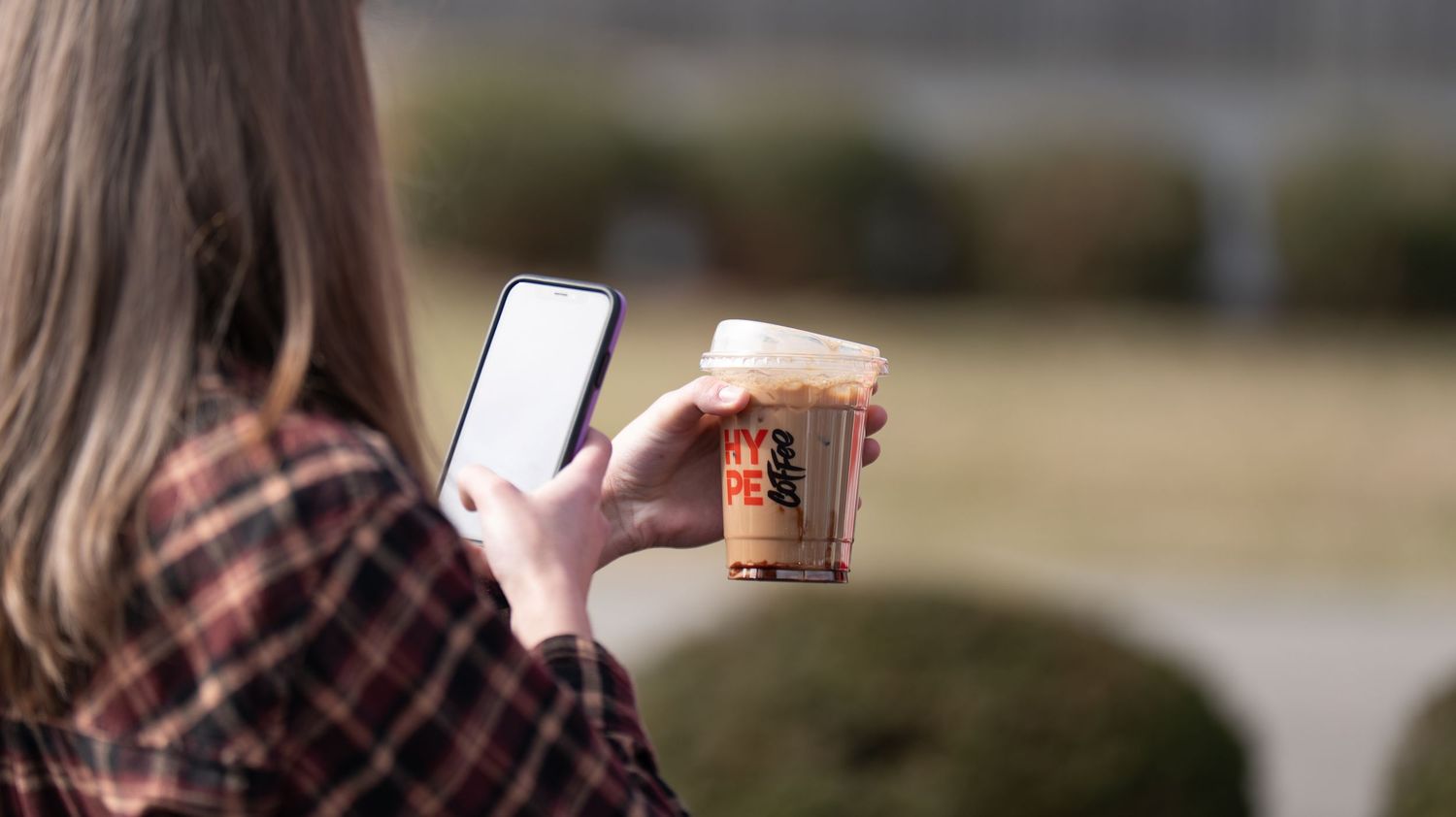 People holding phones and coffee cups while standing outdoors.