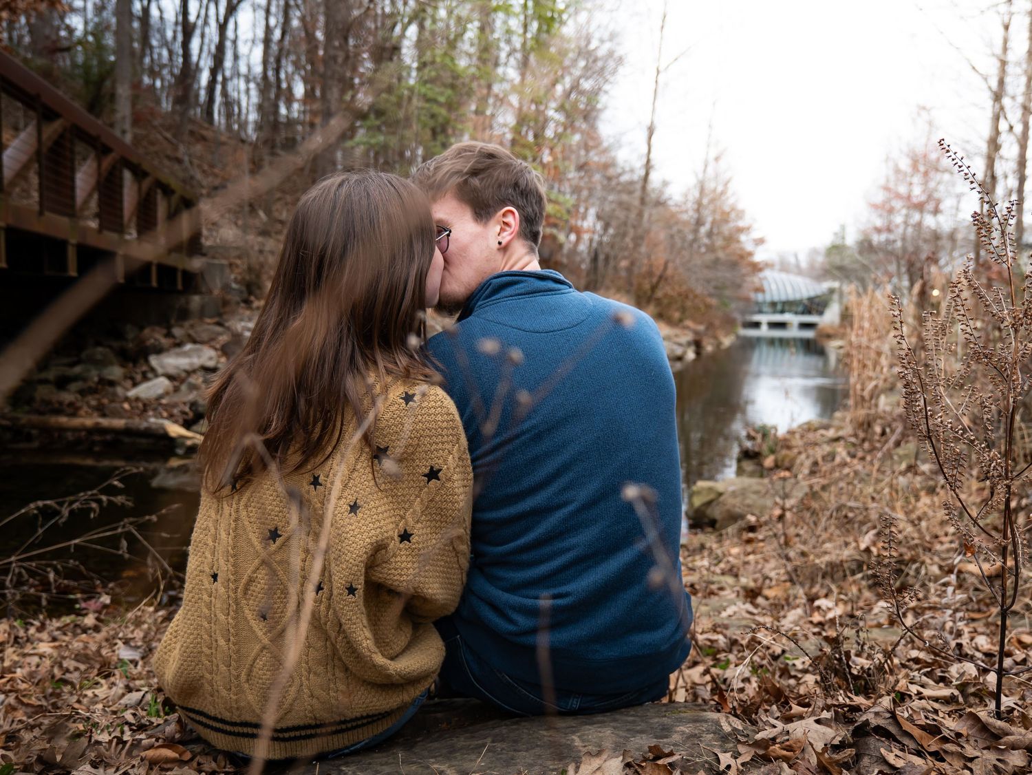 Couple sitting on railroad tracks surrounded by fallen autumn leaves in a romantic outdoor setting.