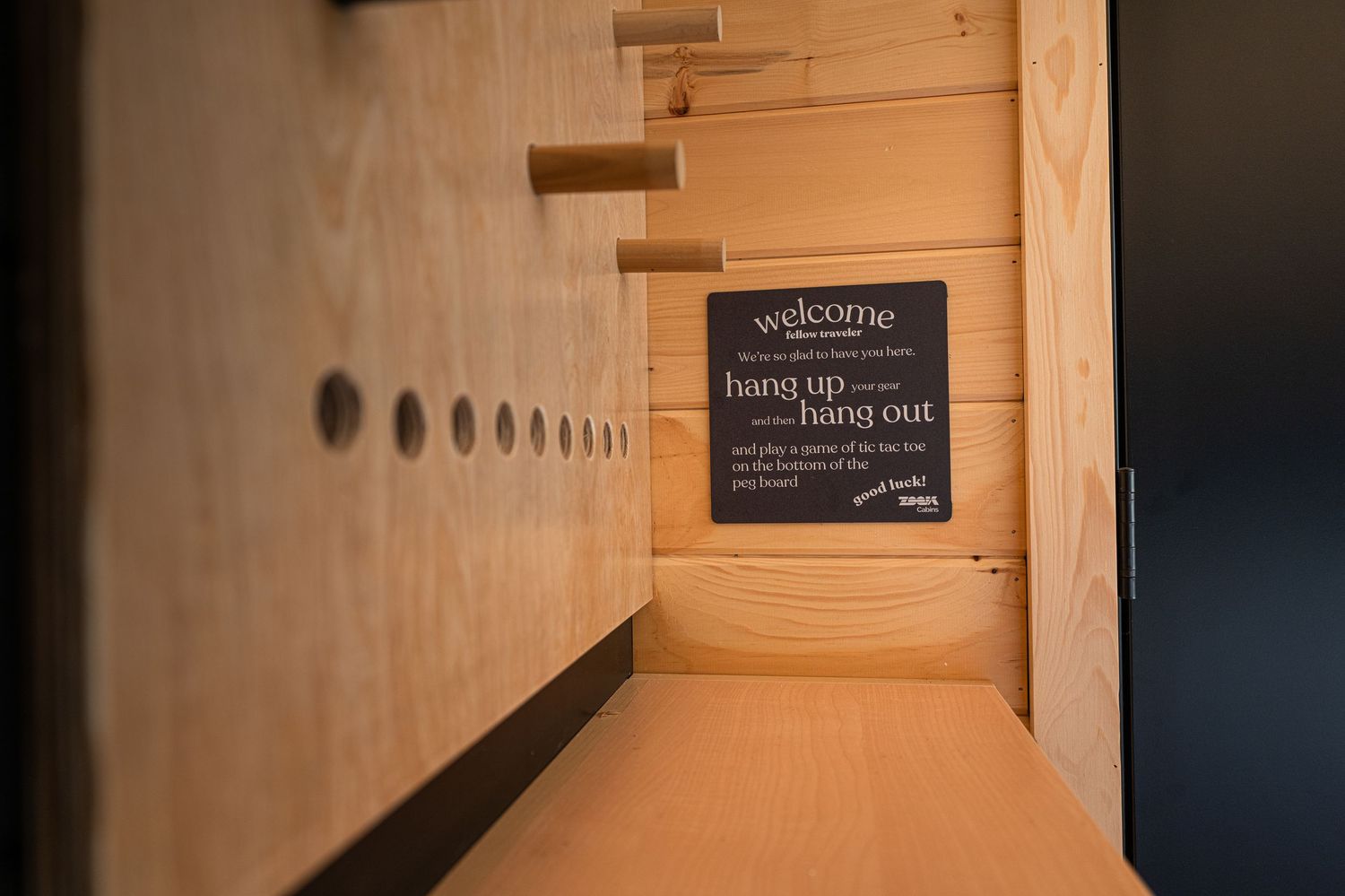 Modern wooden interior hallway with a welcome sign reading hang up and hang out on a dark chalkboard wall.