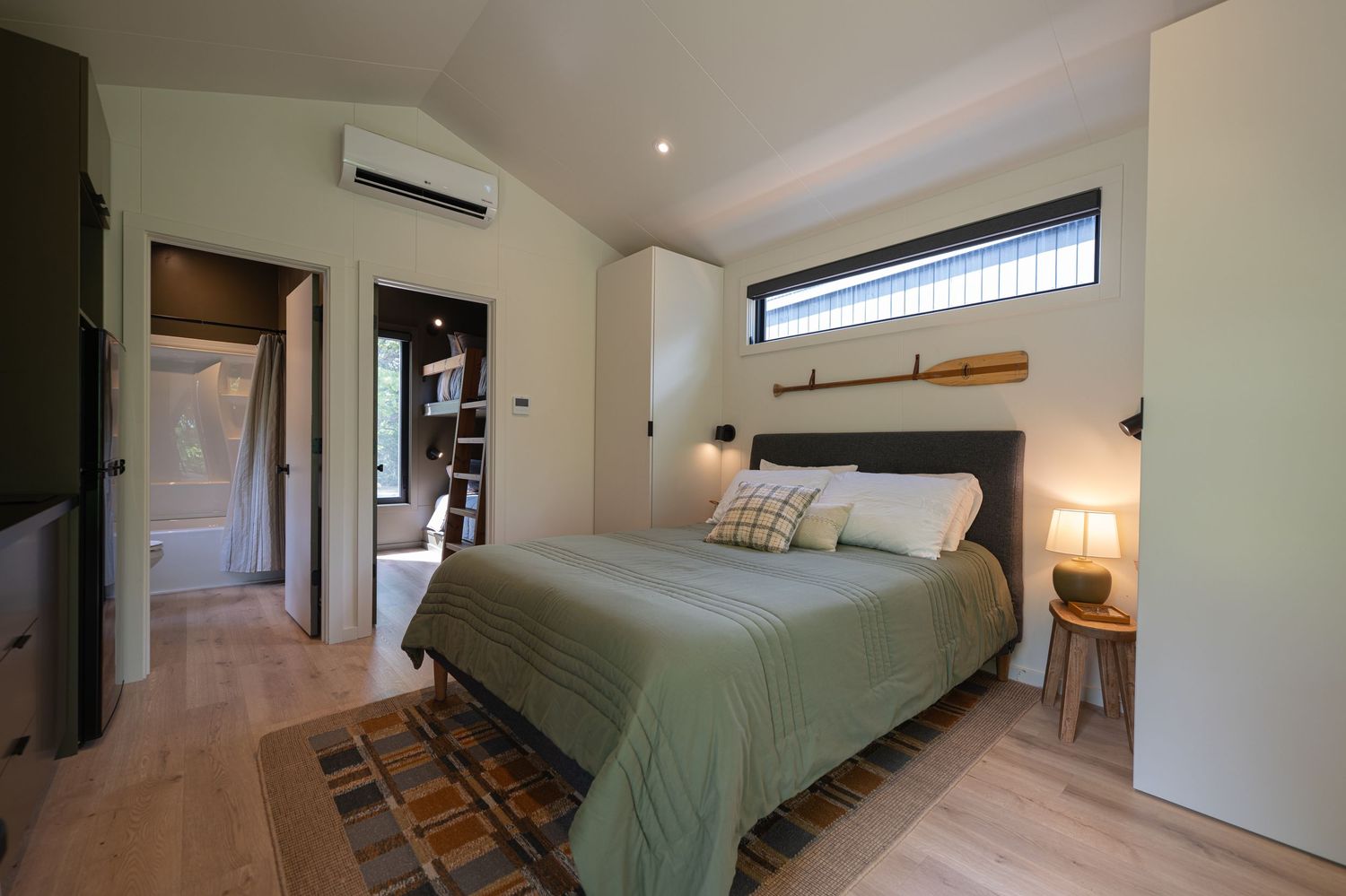 Modern bedroom with green bedding, vaulted ceiling, mini-split AC, hardwood floors, and an ensuite bathroom.