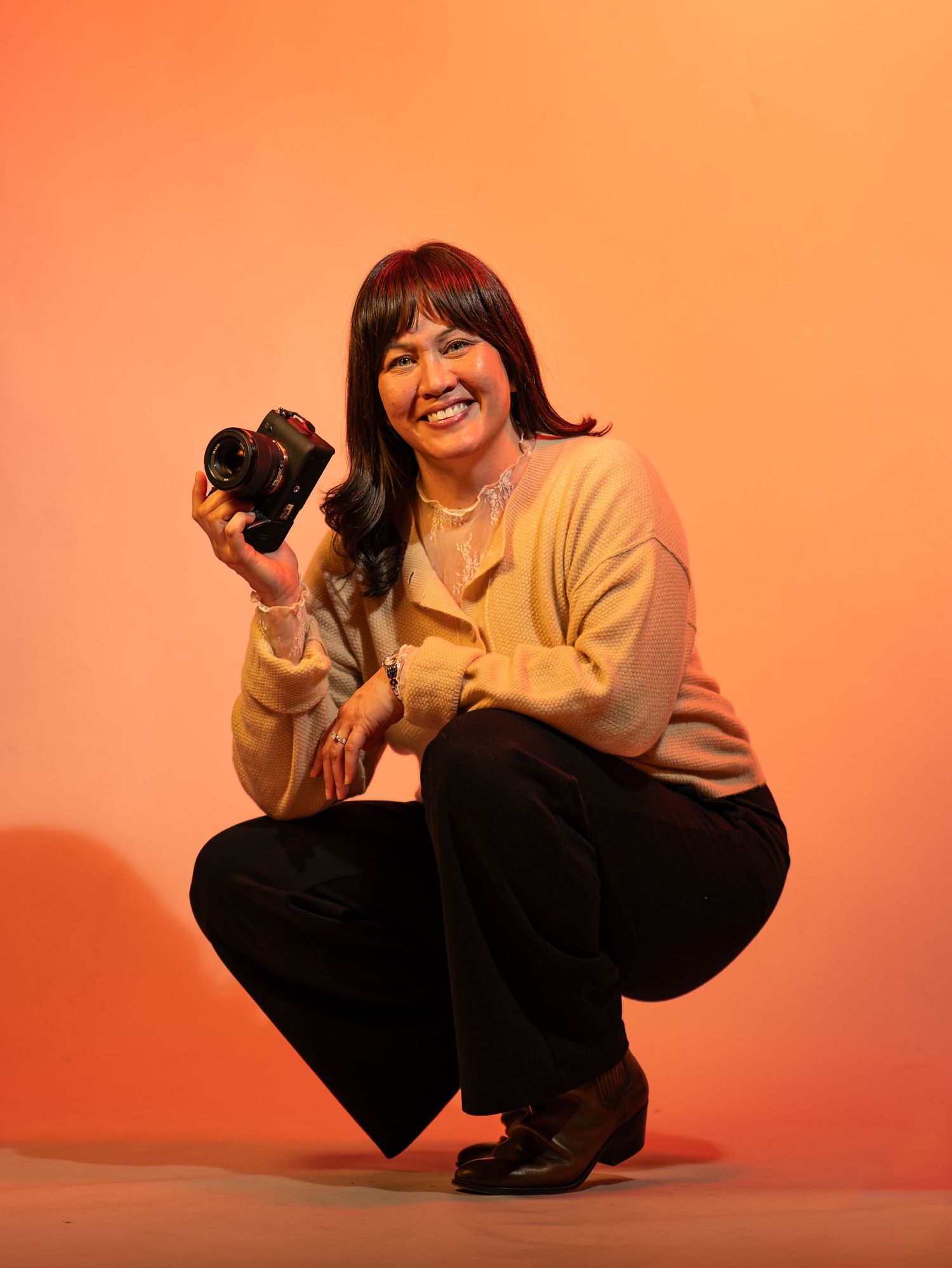 A series of photos showing a photographer in a beige sweater and black pants crouching and posing with a camera.
