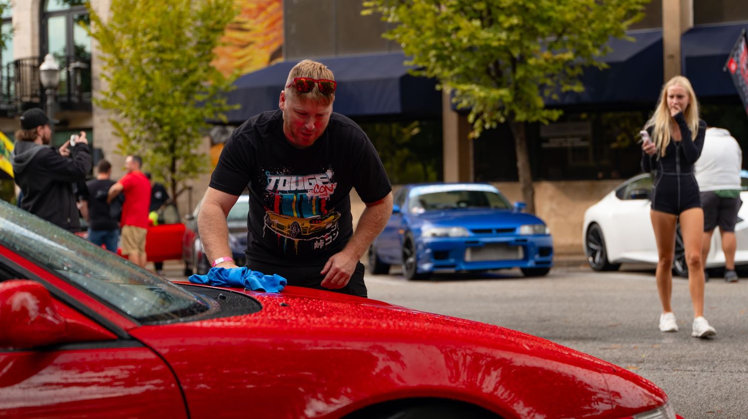 Outdoor scene with yellow trees, red sports cars, and people gathered at a car event.