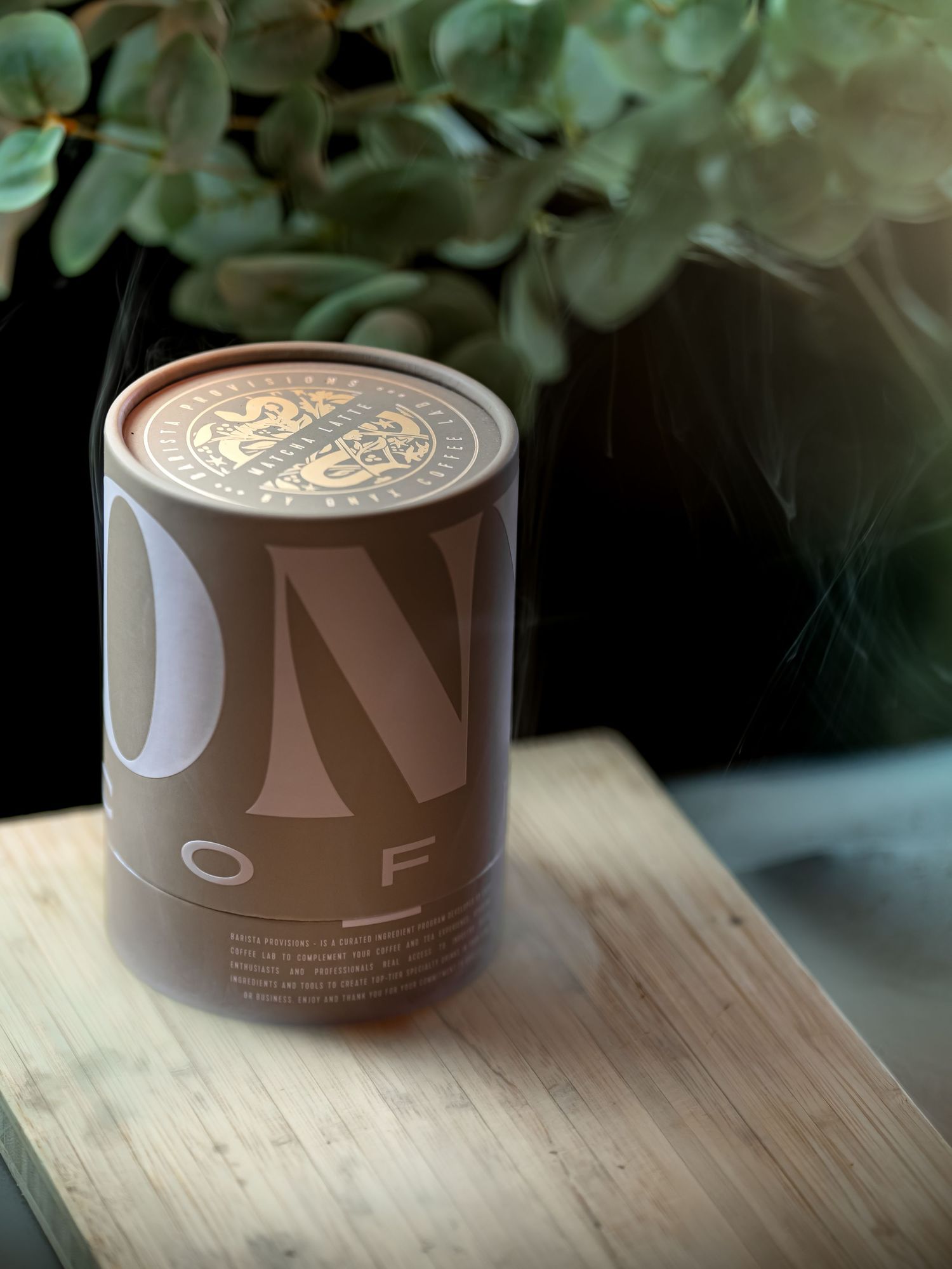 Brown cylindrical product packaging shown from different angles on a wooden surface with green foliage in background.