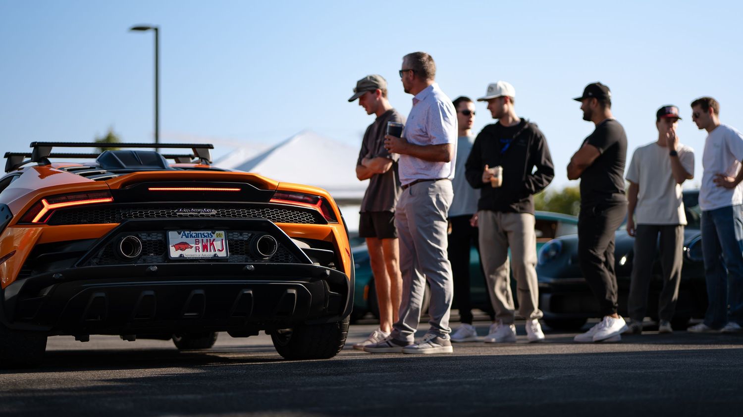 Row of luxury sports cars on display at outdoor car meet with spectators.