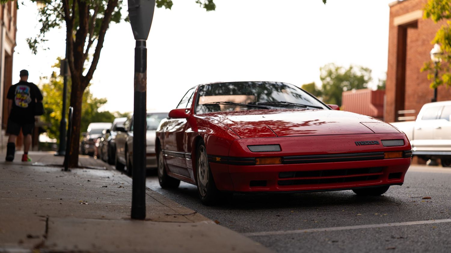 Urban street scene with red vintage cars parked along brick buildings.