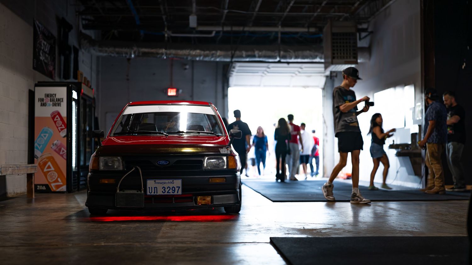 Dark parking garage interior with silhouettes of people and cars visible against bright entrance.