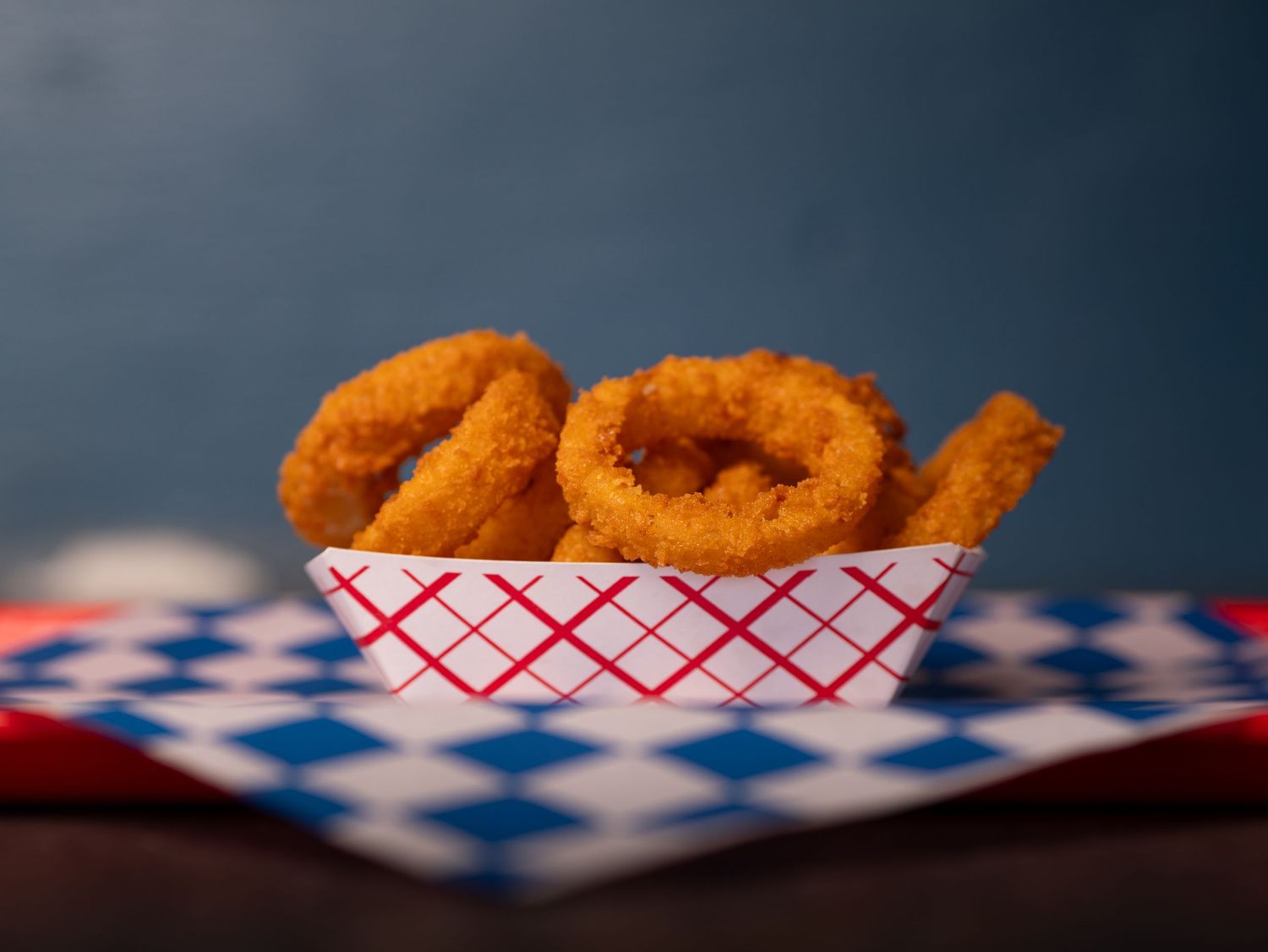 Crispy golden onion rings served in a red and white checkered paper basket.