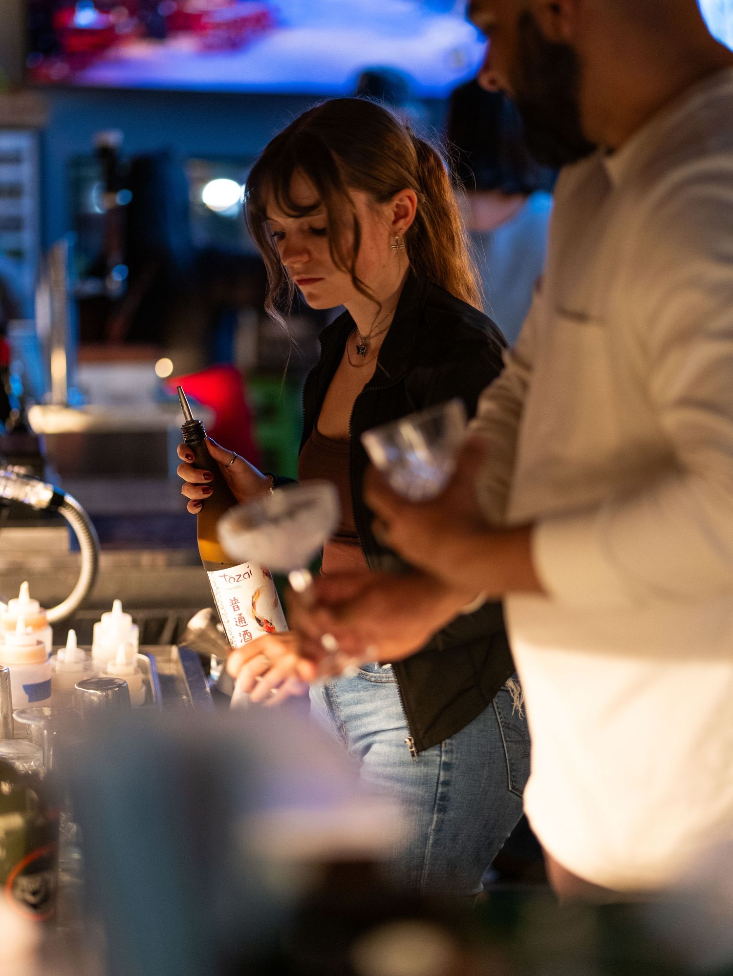 People sitting at a dimly lit bar using their mobile phones while illuminated by soft ambient lighting.