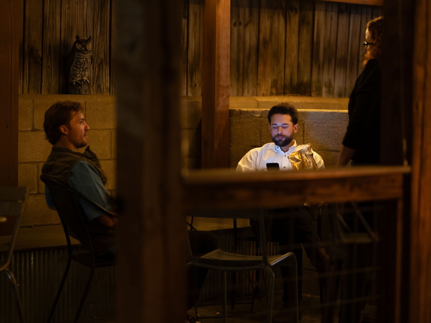 A dimly lit restaurant interior with rustic wood paneling and people dining at tables in the evening atmosphere.