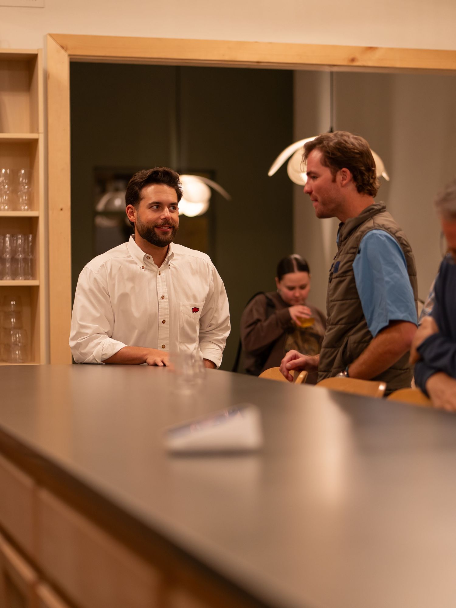 People sitting at a wooden bar counter in a warm-lit restaurant interior having a conversation.