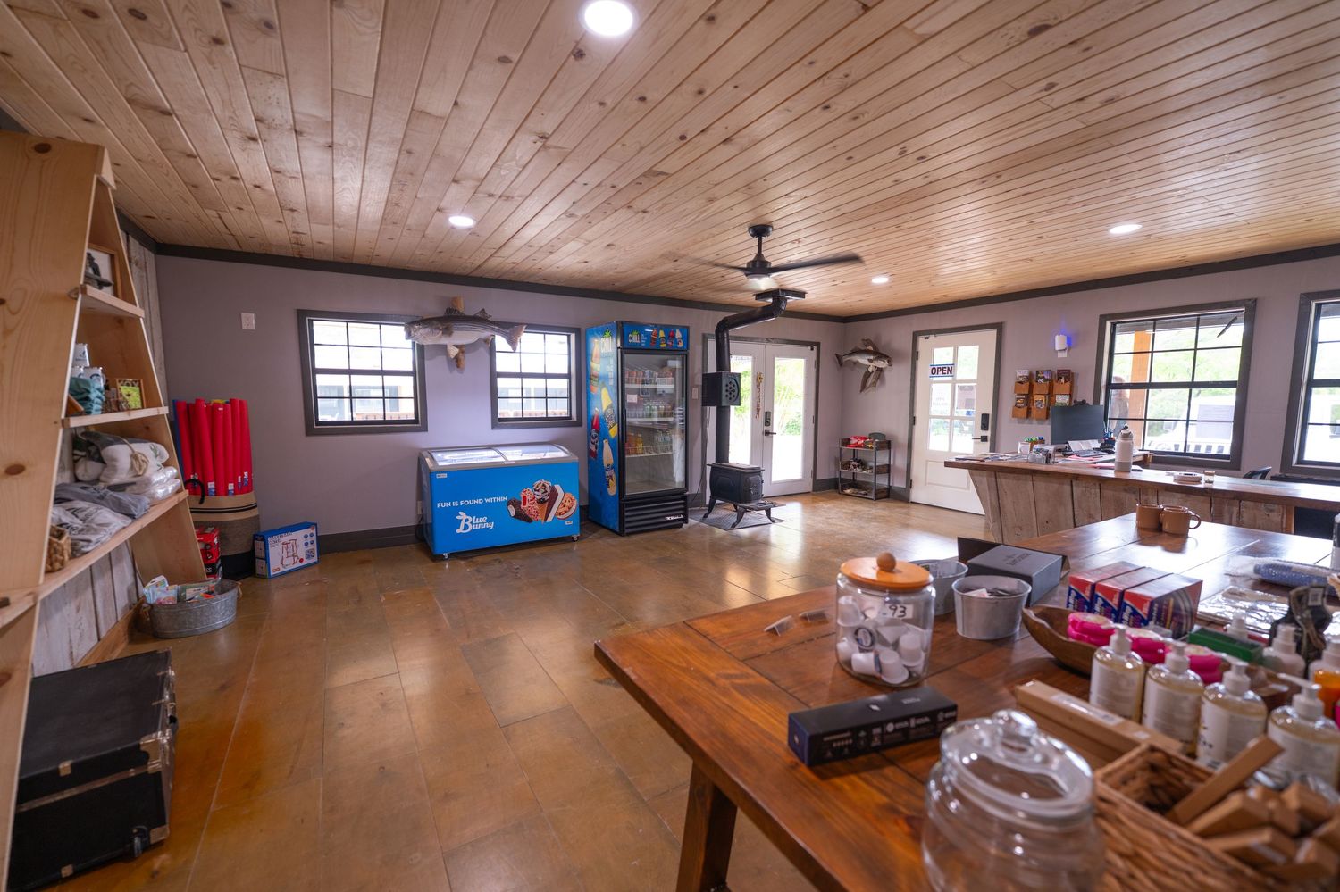 Rustic camp store interior with wood ceiling, ceiling fan, coolers, and merchandise displays on polished concrete floors.