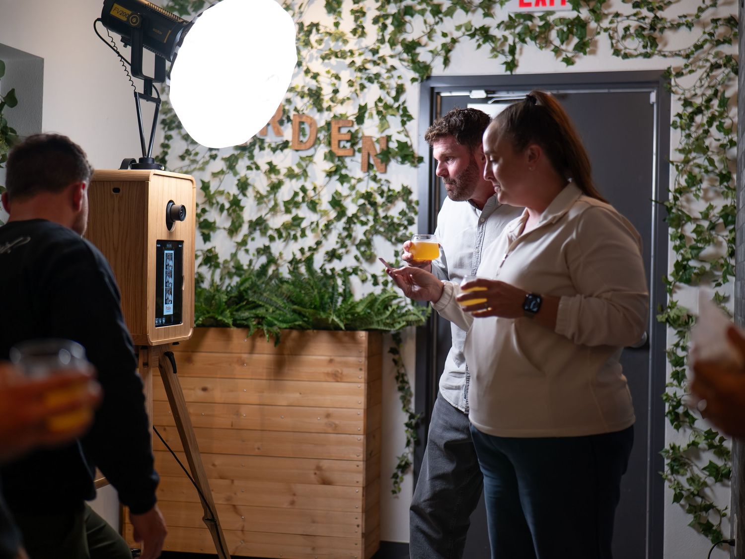 Two people enjoy drinks at a cozy bar with floral wallpaper and wooden accents.