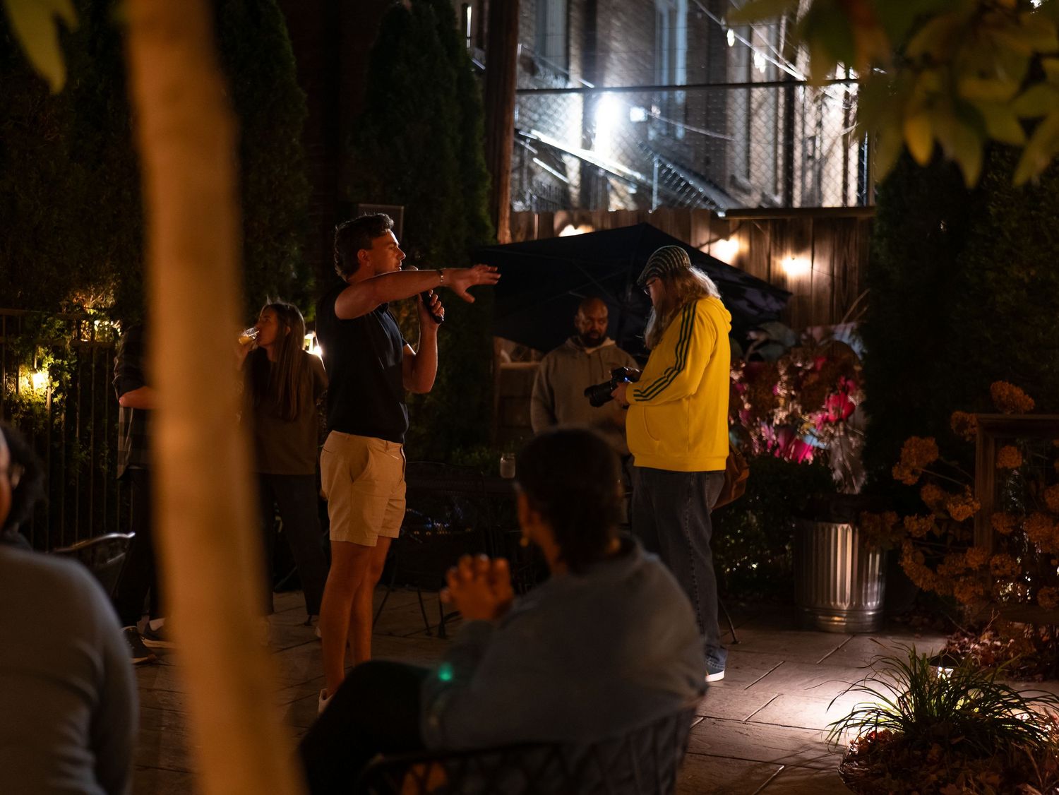 People gather in an outdoor area at night with illuminated string lights creating a festive atmosphere.