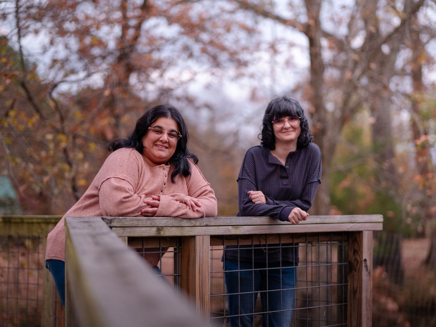 People lean on wooden railing in autumn park setting during outdoor photo session.