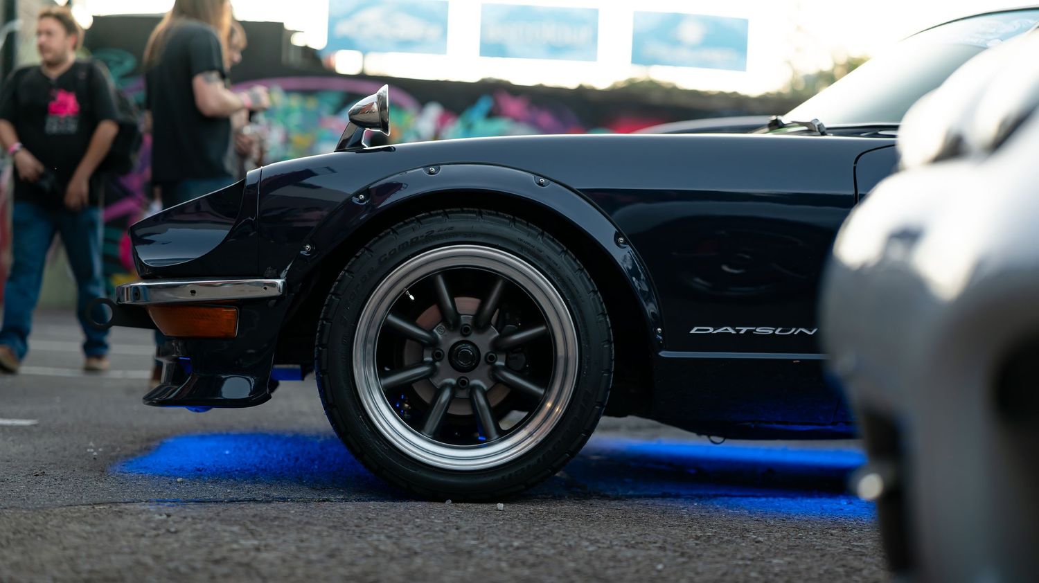 Low-angle shot of modified sports cars displayed on blue protective floor mats at an auto show.