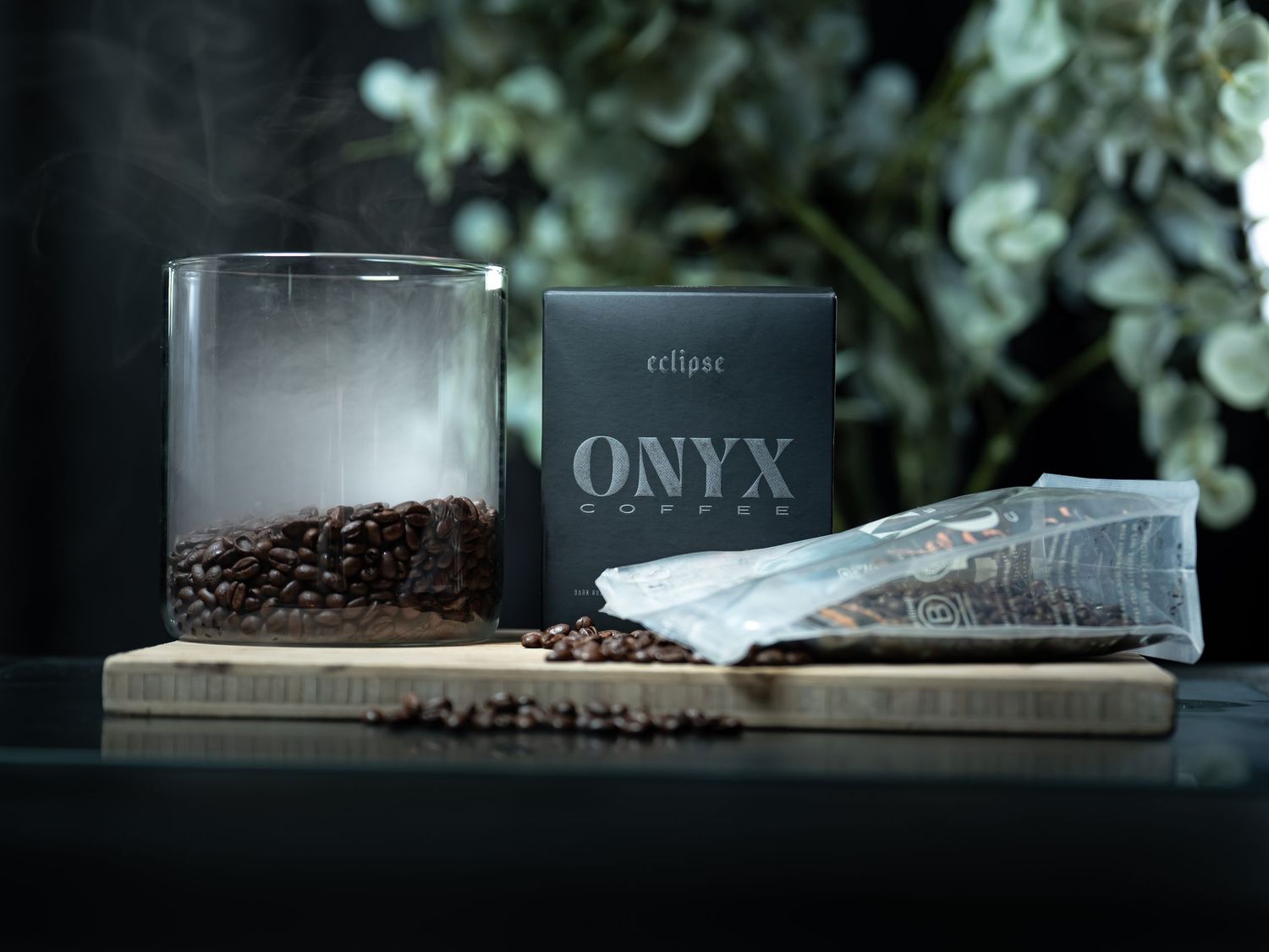 Eclipse Onyx Coffee beans displayed with branded black box, glass tumbler, and packaging on wooden board.