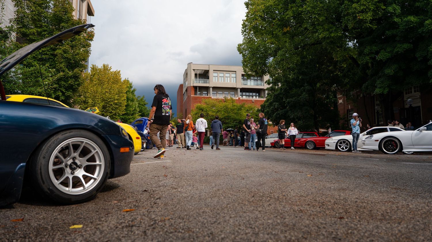 Wide angle view of a parking lot with cars and people gathering for an outdoor event.