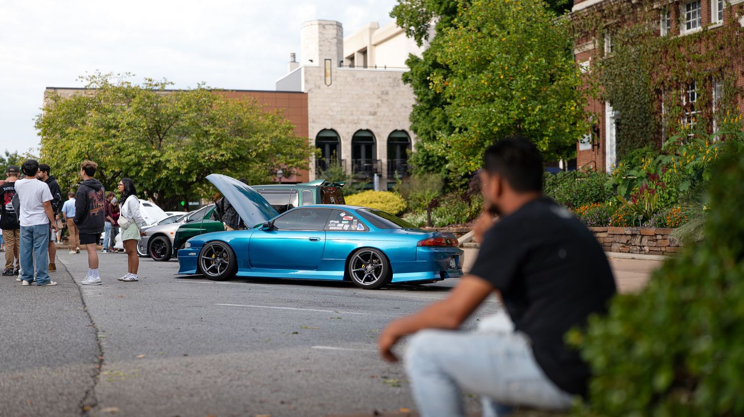 Wide panoramic view of a car meet with various modified vehicles parked along a street.