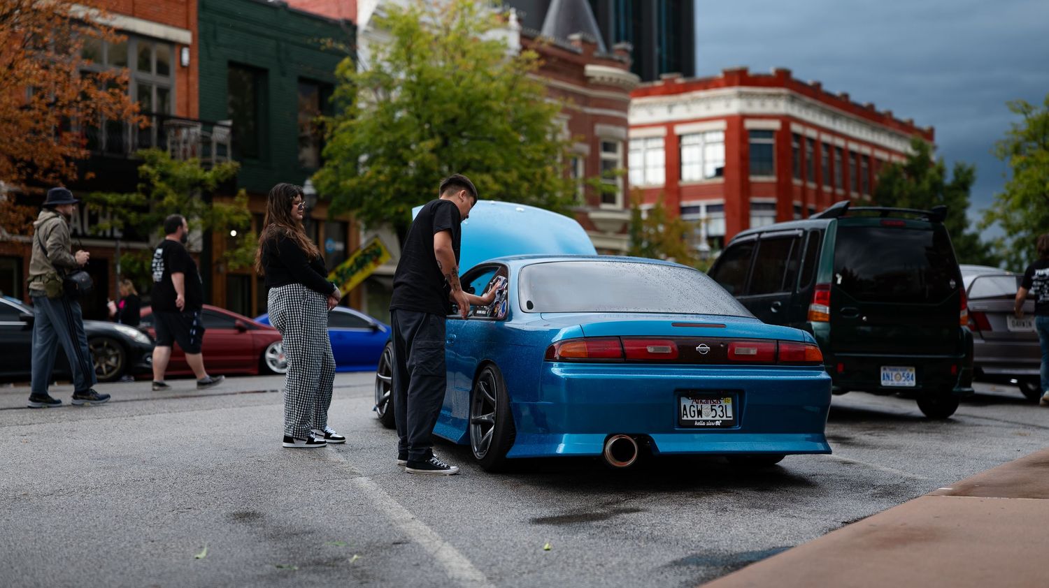 Car show event with classic and modern vehicles lined up in a parking lot at dusk.
