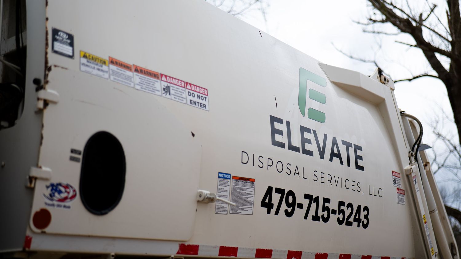 Side view of a white commercial waste management truck with Elevate Services branding.