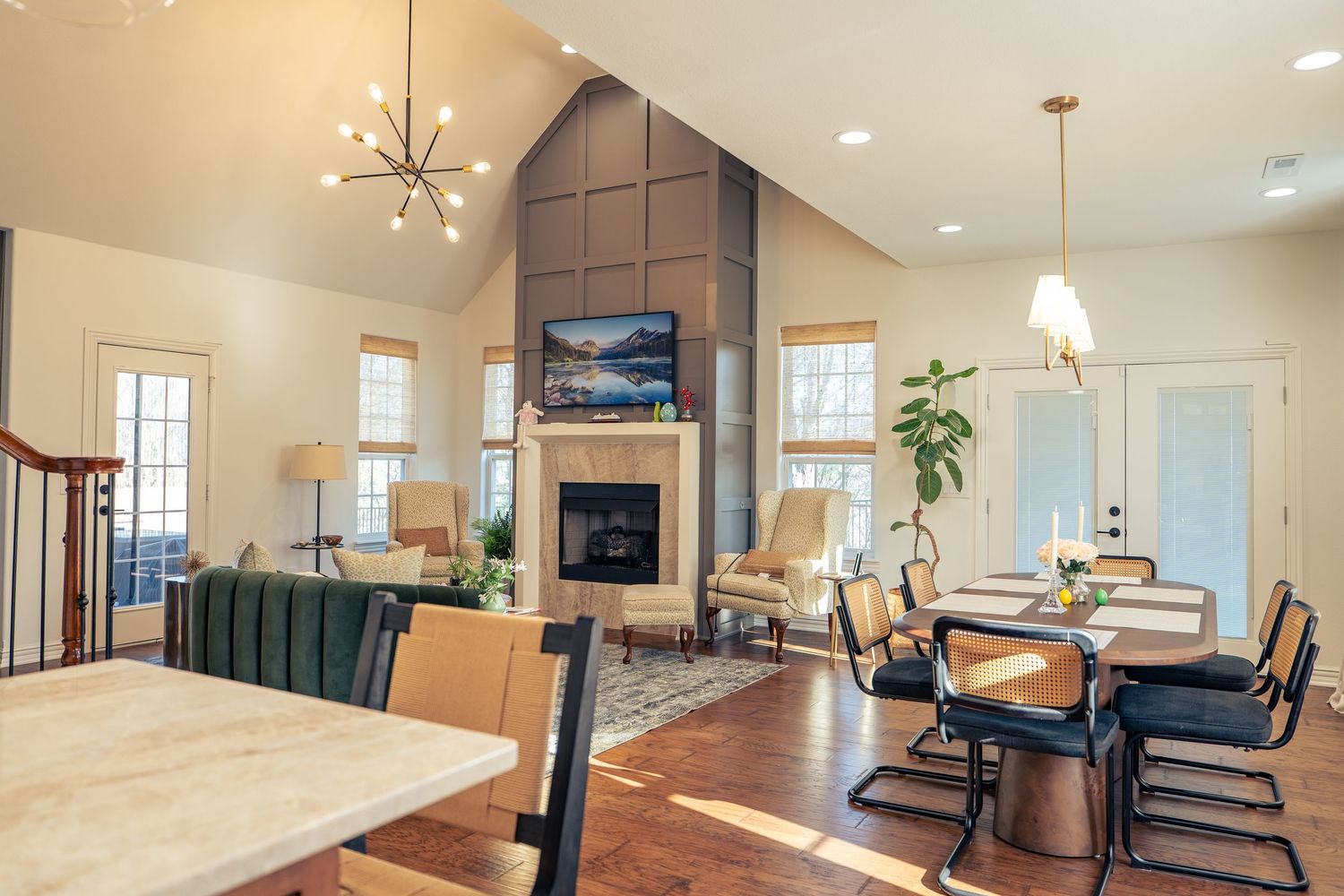 Open-concept living and dining room with vaulted ceilings, modern chandelier, stone fireplace, and hardwood floors.