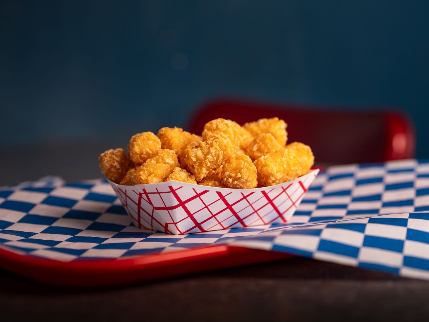 Golden fried popcorn chicken served in red and white checkered paper baskets on a blue plaid tablecloth.