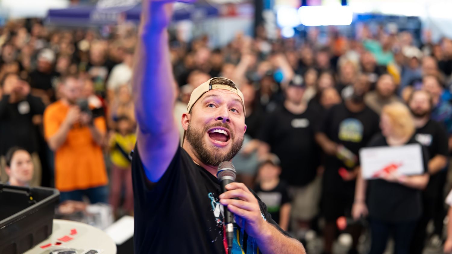 Enthusiastic crowd cheering during an esports event with purple stage lighting.