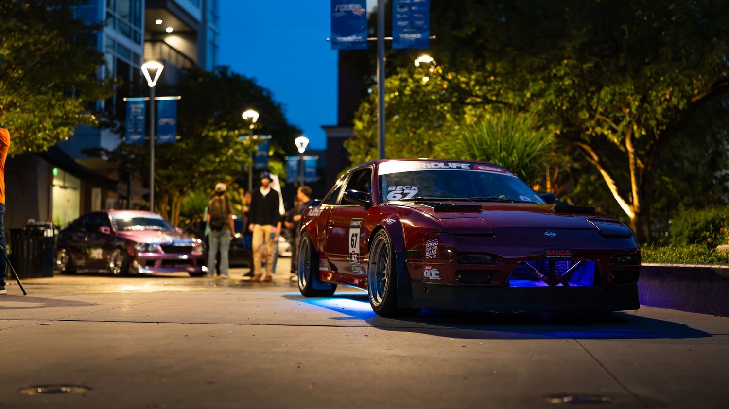 Nighttime street scene with illuminated buildings and parked vehicles.