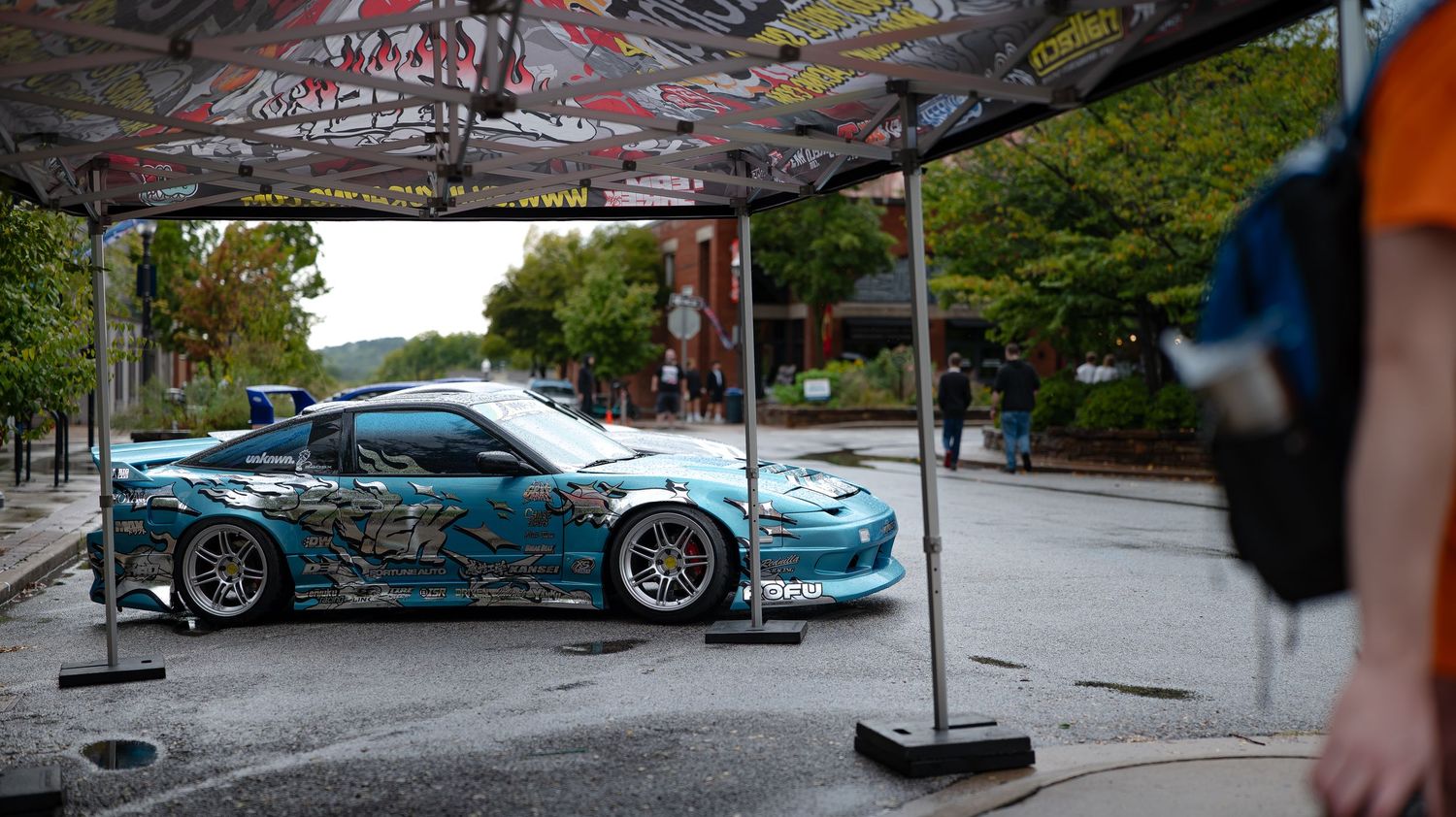 Car show setup with modified vehicles displayed under covered area with graffiti art.