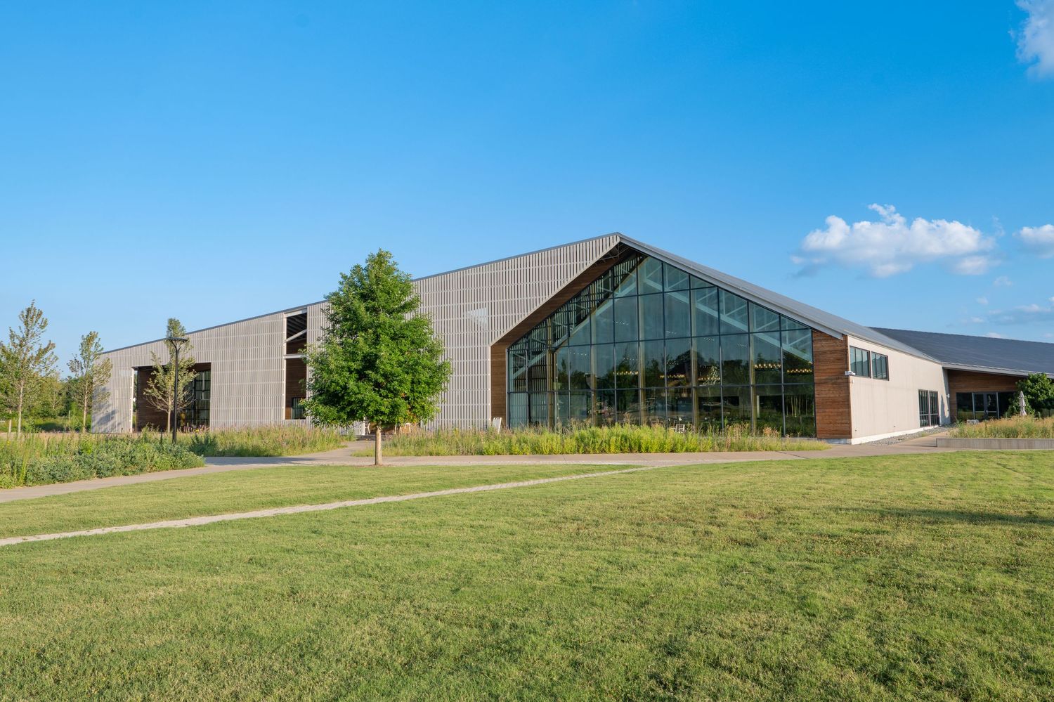 Modern building with large glass facade, metal cladding, and green lawn under blue sky.