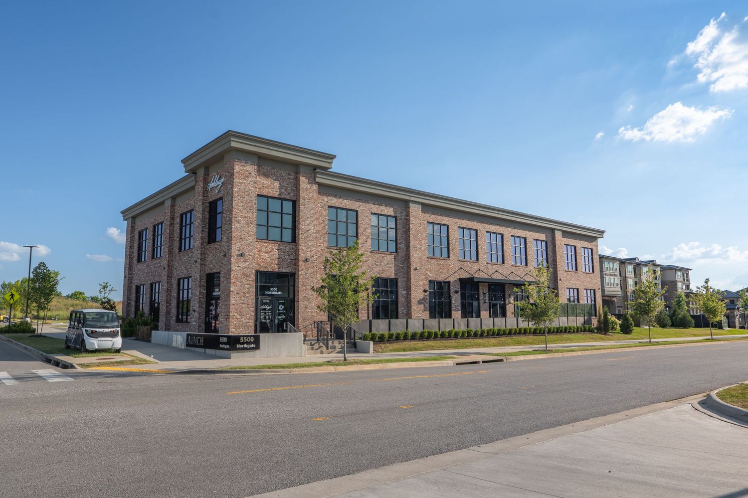 Two-story brick commercial building with large windows on a sunny day, located at a street corner with landscaping.