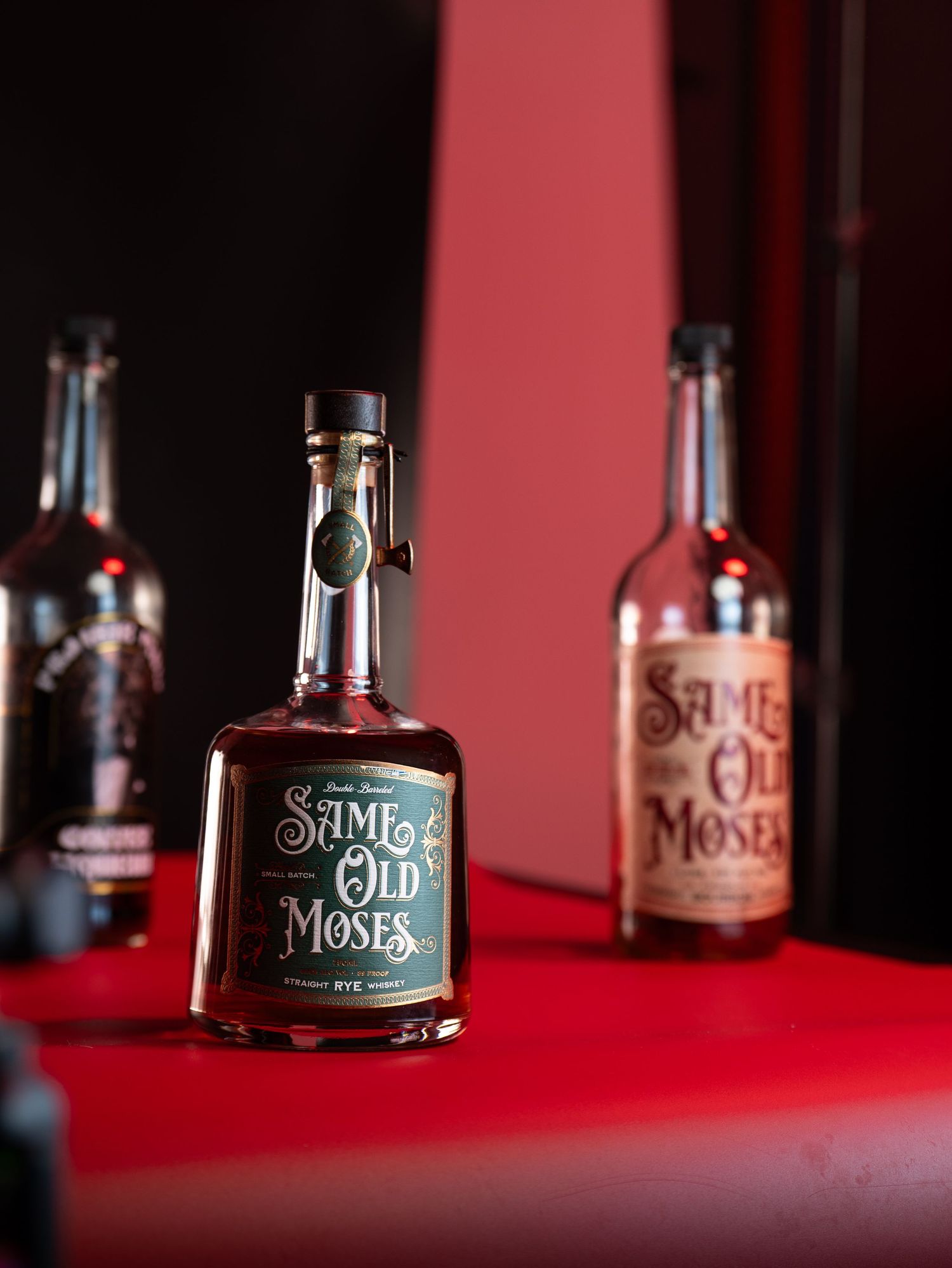 A bottle of Same Old Moses whiskey displayed against a red background in a sequence of four artistic product shots.