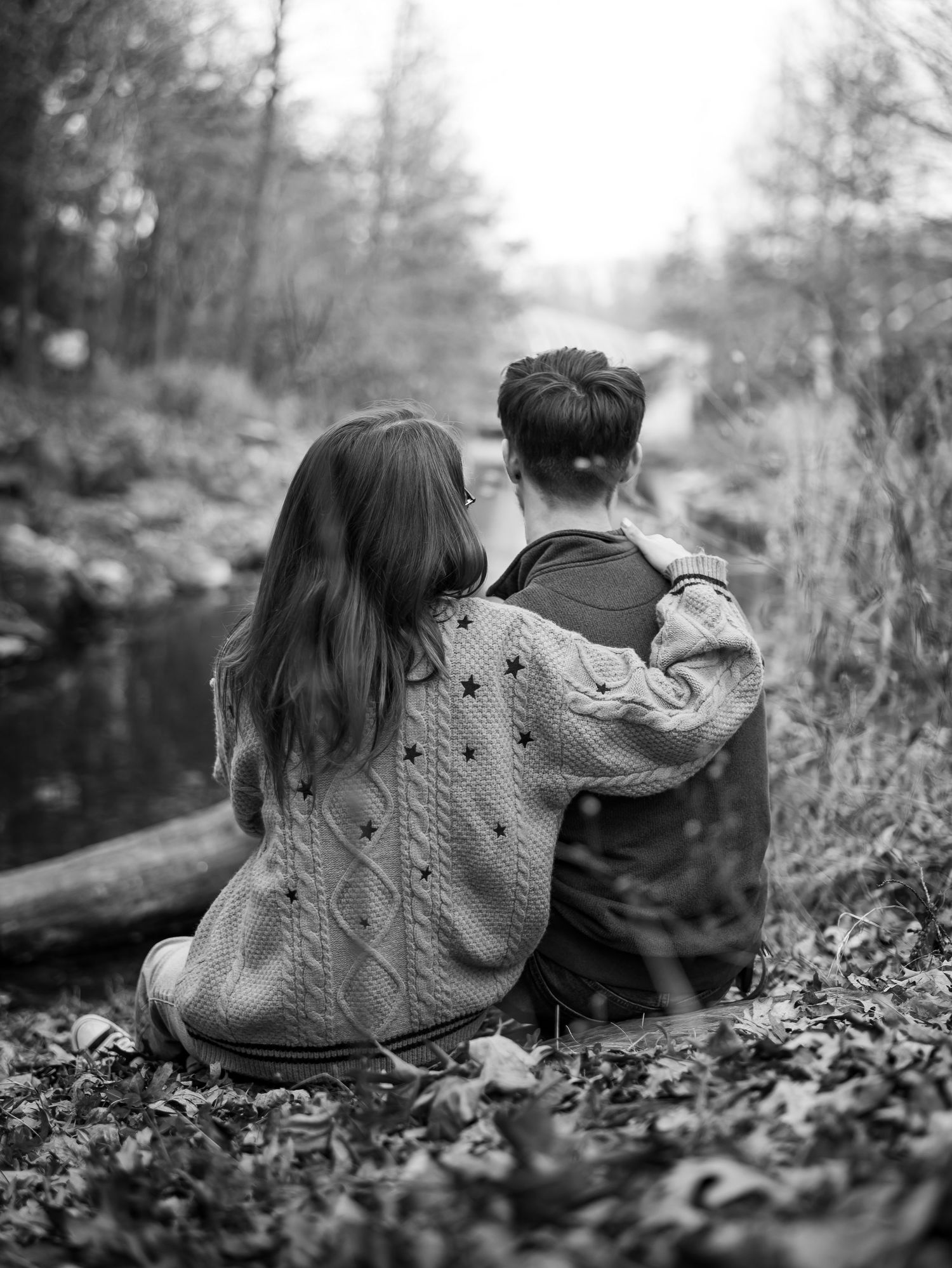 Black and white panoramic sequence showing two people lying in fallen leaves on a forest floor looking upward.